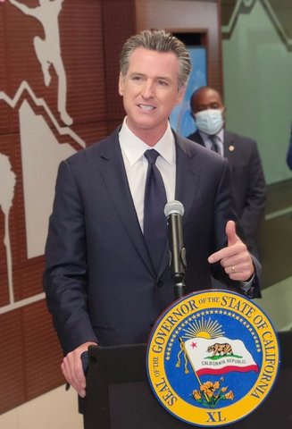 Gavin Newsom at a lectern with a man in a medical mask behind him