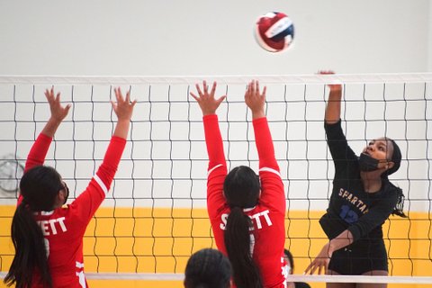 Volleyball game with player in black on one side and two in red on the other, all reaching for red, white and blue ball