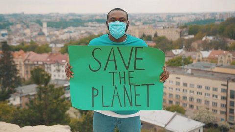 A Black man in a respiratory mask holds a sign that says "Save the planet"