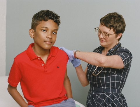 Boy in polo shirt with female medical worker preparing his arm for a shot