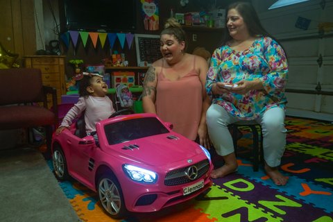 A smiling little girl in a pink play Mercedes looks at her mom and grandmother in their garage, which has been converted into a play area.