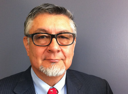 Head and shoulders shot of a man with dark but graying hair, a white beard, glasses and a suit.