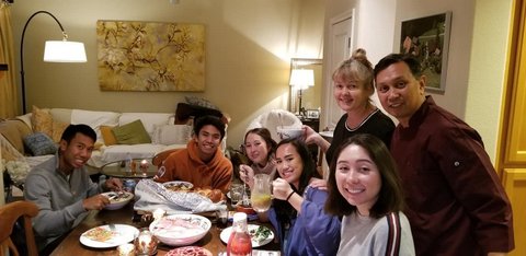 Two young men and four young women sitting at a table for Thanksgiving dinner with a man and woman standing beside them.