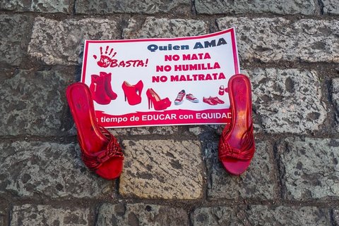 Sign with message in Spanish that reads"quien ama no mata no humilla no maltrata" sits between a pair of red shoes