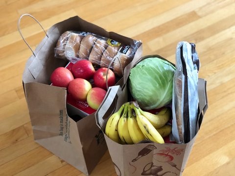 Two brown paper bags of groceries seen from above. Bananas, apples, bagels and a head of iceberg lettuce are on top.