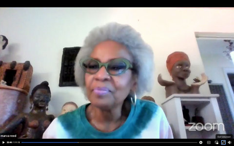 Black woman with gray hair, green glasses and pink lipstick. Artwork including two busts of Black women is behind her.
