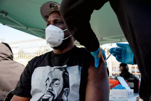 A Black man wearing an N95 mask receiving a vaccine shot.