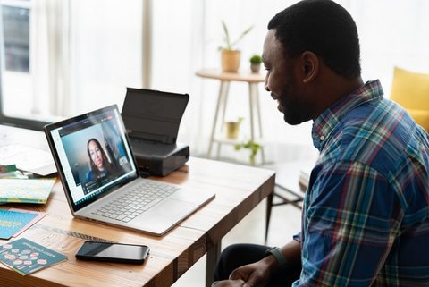 Side view of a Black man looking down at his laptop screen, engaged in a video call with a Black woman