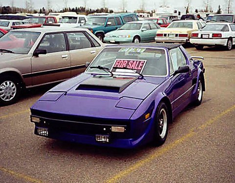 Purple sports car with for sale sign in lot with other cars