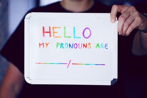 Person holding up whiteboard with "Hello my pronouns are" written in colorful lettering