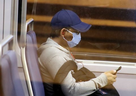 Side view of passenger seated on train wearing a baseball cap and mask