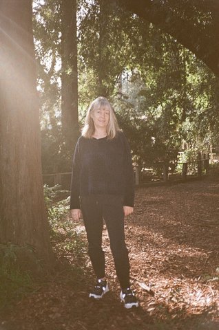 Blonde woman standing among trees on nature trail with sunlight streaming in