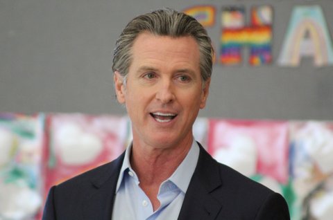 Gov. Gavin Newsom with colorful artwork out of focus on the wall behind him because he is at an elementary school