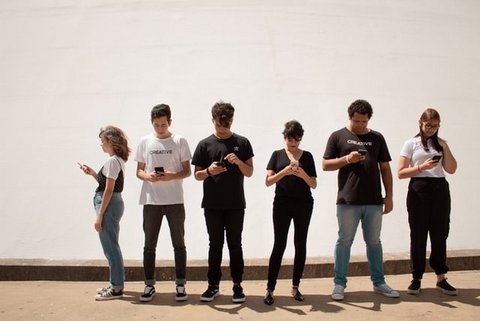 Six young people in a row all looking at their phones