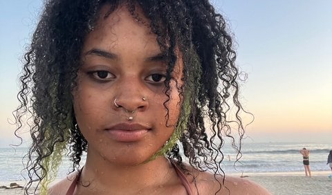 Close-up of a young Black woman with curly hair and piercings on her nose and upper lip standing on a beach