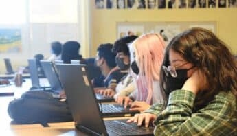 A row of high school students wearing masks and looking at laptops