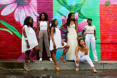 Six Black women in front of colorfully painted brick wall