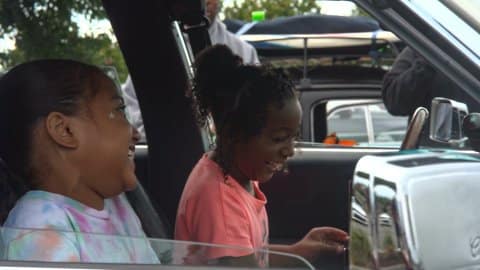 Two little girls laughing in the front seat of a parked car