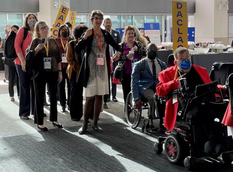 A group of people, some standing and some in wheelchairs, some wearing masks and some not