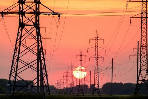 Electric towers and wires at sunset. The sky is an orange color, and the is large and low in the sky.