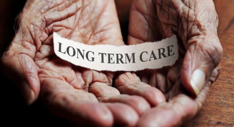 What looks like a scrap of paper with the words "long term care" sits in a Black person's cupped, wrinkled hands