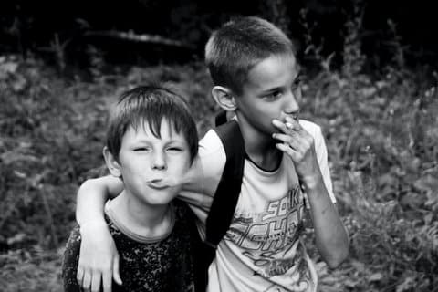 Black-and-white photo of two young boys. One is holding a cigarette to his lips. The other is blowing smoke as he looks at the camera.