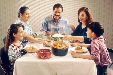 Two women, a man, a girl and a boy, all smiling, are sitting at a table filled with food.