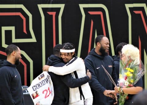 A Black teen boy hugging a Black man. Standing by them are two other Black men and a Black woman with blonde hair holding a bouquet of flowers.