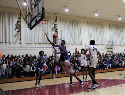 In a high school boys basketball game, some players are in or near the paint, one is falling backward and two are airborne as one drives for the basket
