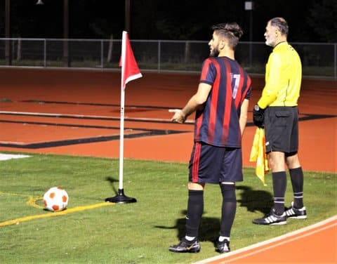 A soccer player stands next to a referee before taking a corner kick