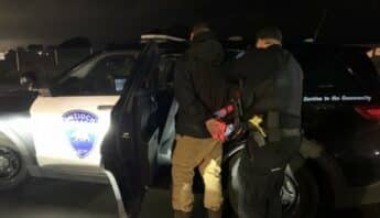 Police officer putting handcuffed man into Antioch Police car.