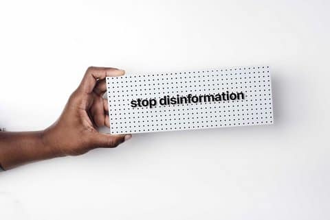 A Black person's hand holding a sign that reads "stop disinformation"