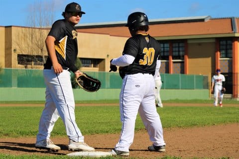 Two players at first base in high school baseball game. They are teammates and wearing the same uniform but playing as opponents.