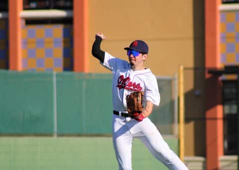 A teen boy in a white Oilers baseball uniform cocks his arm to throw the ball
