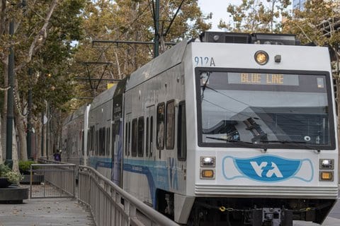A blue line Valley Transit Authority light rail train. A medical mask is painted on the front of the train.
