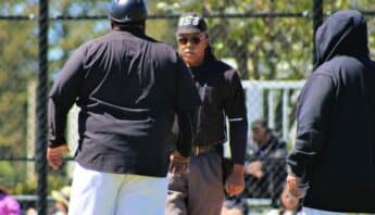 An umpire and coach facing each other with another man standing by