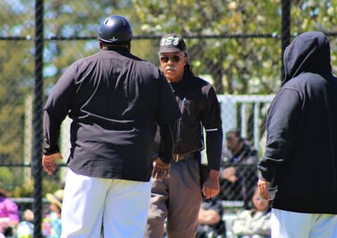 An umpire and coach facing each other with another man standing by