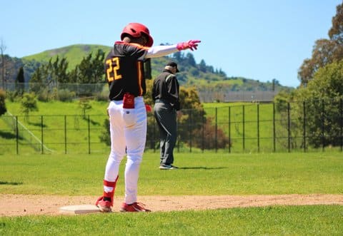 A high school baseball player points while standing on a base after a steal