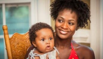 A smiling Black woman holding a Black baby with a surprised look on their face