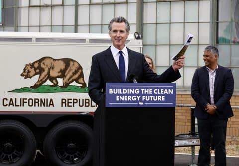 Gov. Gavin Newsom at lectern that says "building the clean energy future" in front of an illustration of the California state flag, which depicts a bear with the words "California Republic"