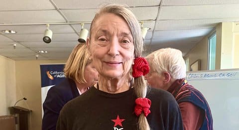 An older white woman with long hair in a side ponytail secured with two red scrunchies