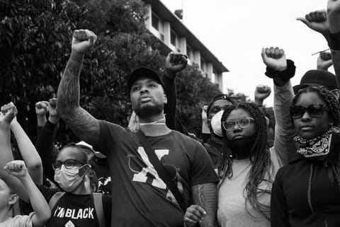 Black-and-white photo of basketball player Damian Lillard and other Black people, each standing with a fist raised in protest.