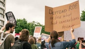 Person in a crowd of protestors holds up sign that says "Defend Roe or lose what took generations to gain"