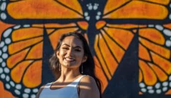 A smiling Latina in front of a large painting of a monarch butterfly.