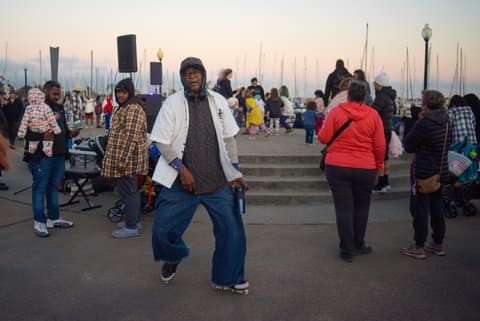 An older Black man on roller skates at dusk among a crowd