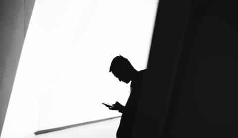 Silhouette of a man looking down at a smartphone