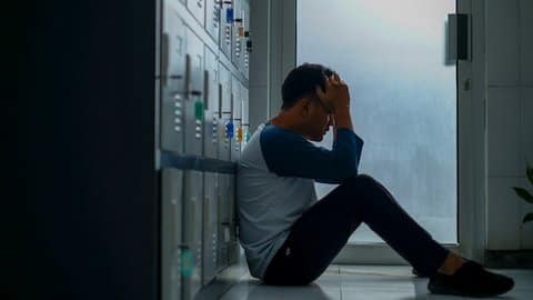 A young man sitting on the floor against a bank of lockers with his head in his hands