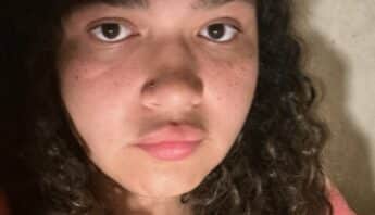 Close up of teenage girl who is mixed Black and white. She has long, curly hair and a serious expression on her face