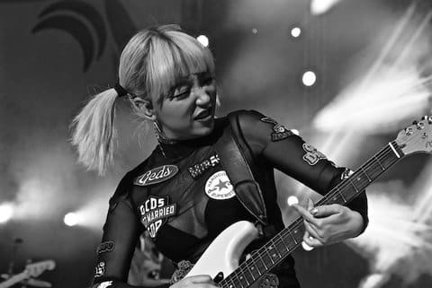 Black and white photo of a woman with short blond hair in pigtails playing electric guitar