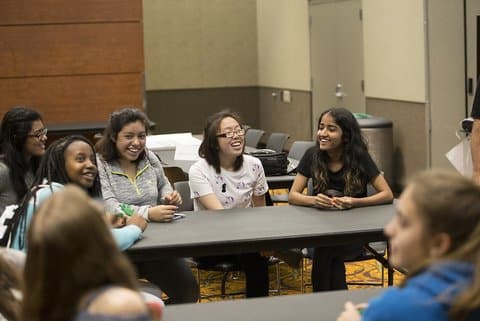 Teenage girls of color sitting at a table and smiling
